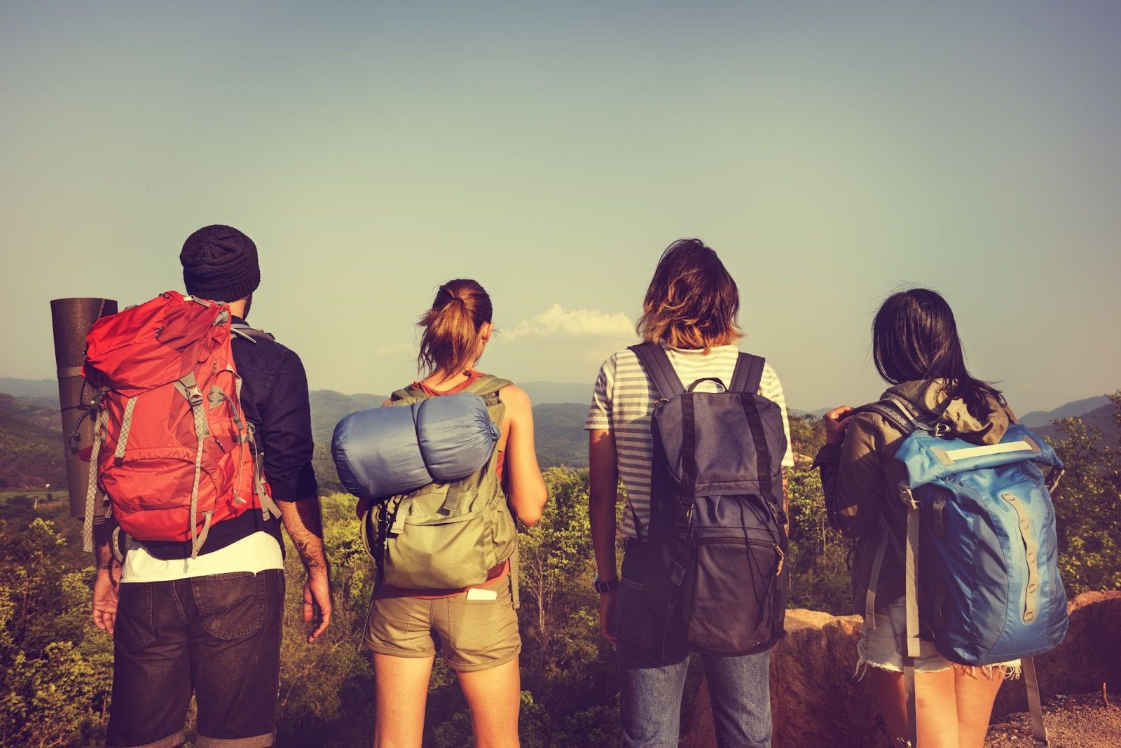 Four people with backpacks standing on a hilltop, overlooking mountains.